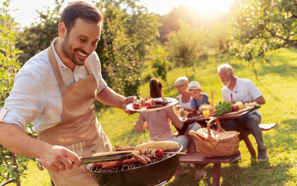 uomo che griglia e famiglia seduta a tavolo da pic nic